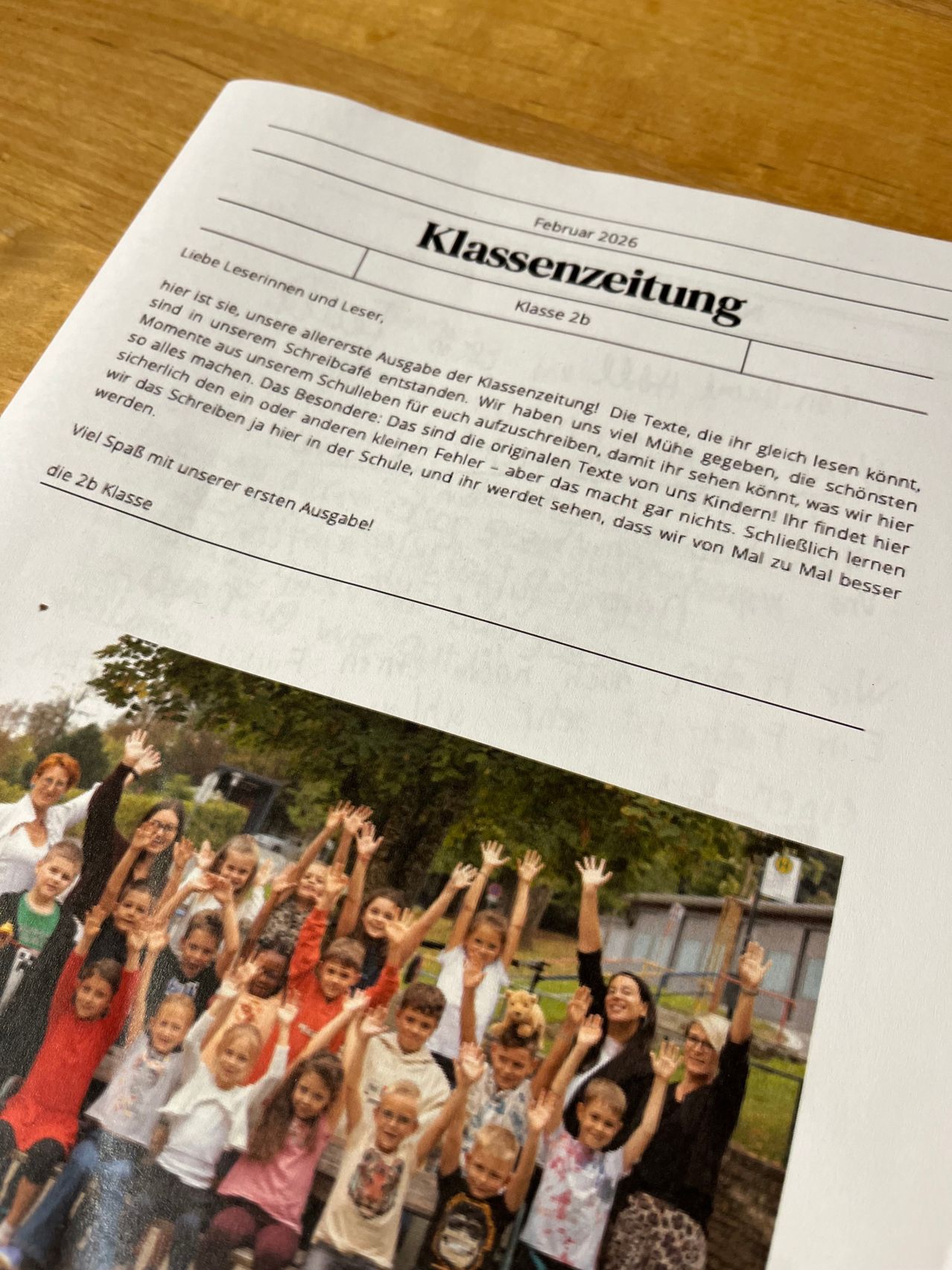 Class newsletter from February 2026 features a photo of a classroom with children waving. The article is for class 2b. It includes texts for reading practice.