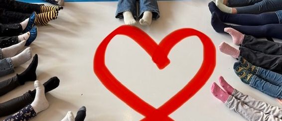 Eine Gruppe von Kindern, die in einem Kreis sitzen und Socken tragen, bilden ein rotes Herz auf dem Boden.