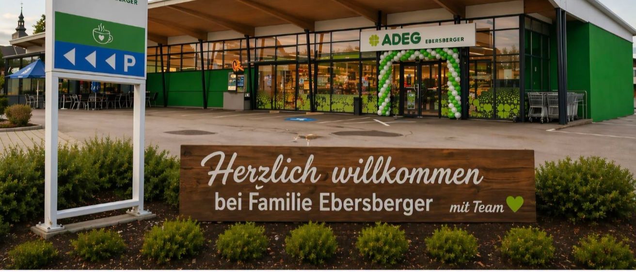 Die Vorderseite eines modernen Supermarktes mit einem Willkommensschild, das Herzlich willkommen bei Familie Ebersberger steht. Der Laden hat ein grünes und weißes Farbschema.