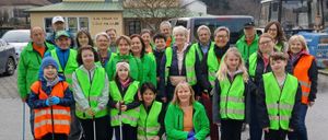 Eine Gruppe von Menschen in grünen Westen und mit Stöcken posiert für ein Foto vor einem Haus und Bäumen.
