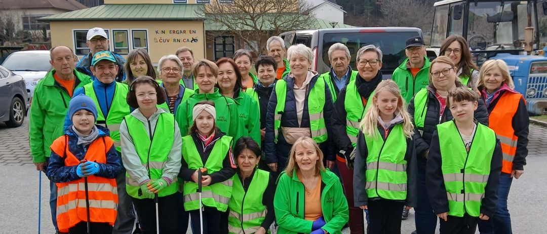 Eine Gruppe von Menschen in grünen Westen und mit Stöcken posiert für ein Foto vor einem Haus und Bäumen.