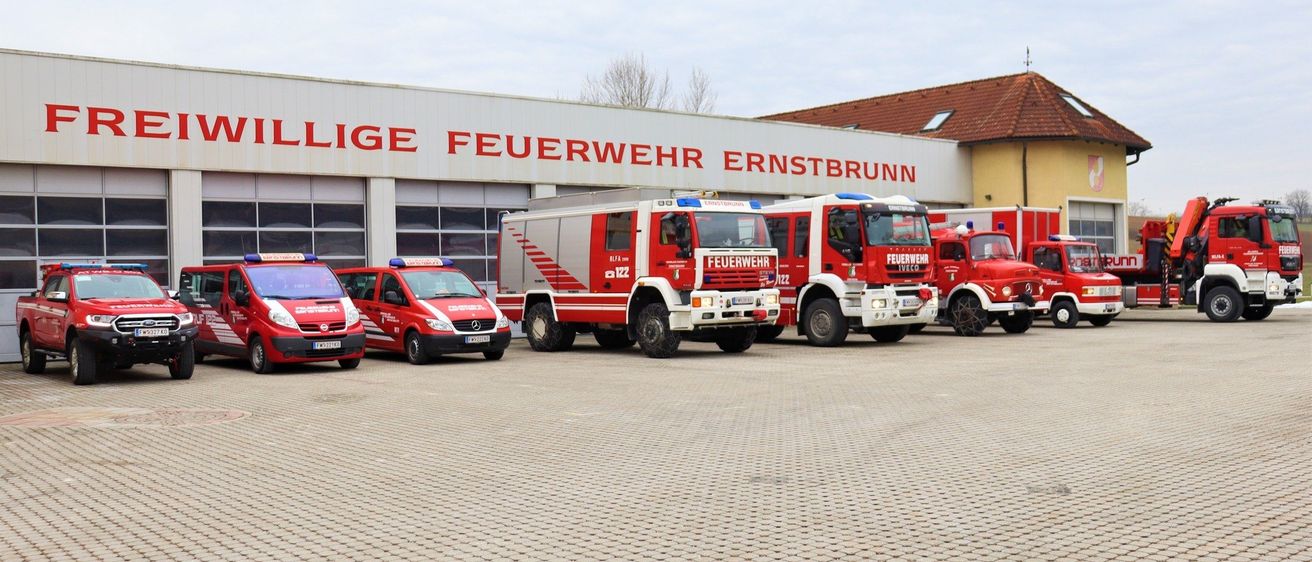 Rote Feuerwehrwagen vor der Feuerwache Ernstbrunn unter einem bewölkten Himmel geparkt.