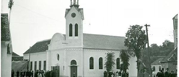 Ein Schwarz-Weiß-Foto einer Kirche mit Turm und Uhr, umgeben von Menschen und Bäumen.