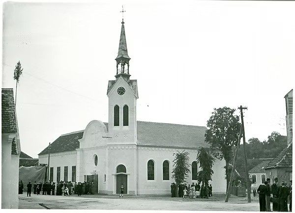 Ein Schwarz-Weiß-Foto einer Kirche mit Turm und Uhr, mit Menschen, die sich draußen versammelt haben.