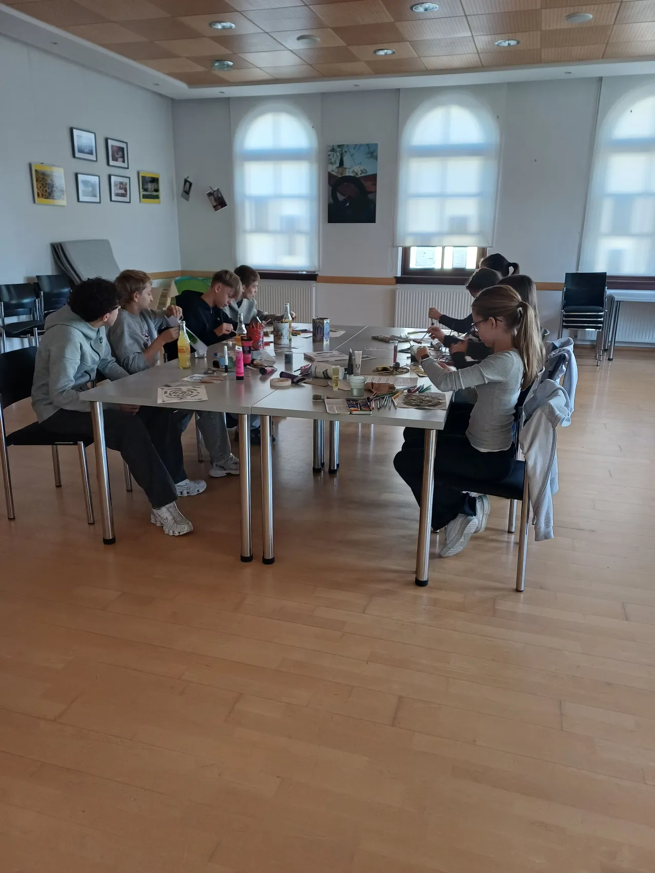 Eine Gruppe von Kindern sitzt um einen Tisch in einem Raum und macht Kunstaktivitäten.