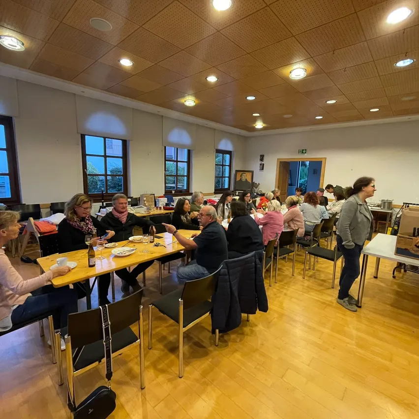 Eine Gruppe von Menschen sitzt an Tischen in einem Raum, möglicherweise bei einer Besprechung oder einem gesellschaftlichen Treffen.