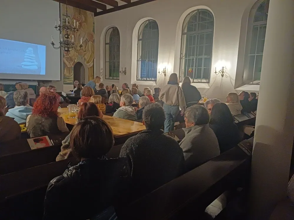Eine Gruppe von Menschen sitzt in einem Raum mit einer Projektionsleinwand, die einen Stapel Steine zeigt.