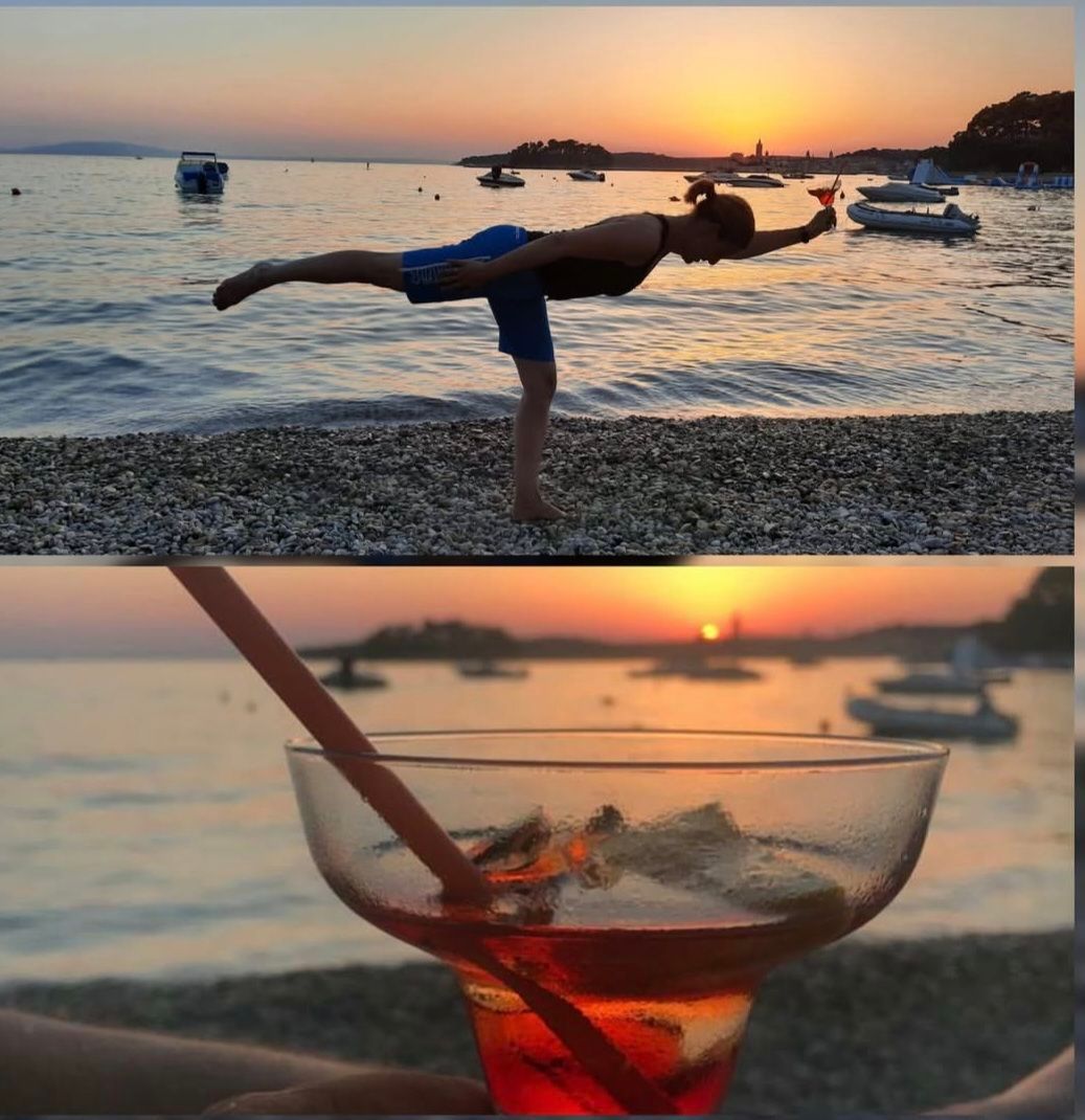 Eine Frau praktiziert Yoga auf einem Kiesstrand bei Sonnenuntergang mit einem Cocktail in der Hand und einem Glas mit rotem Getränk, Eis und Strohhalm im Vordergrund.