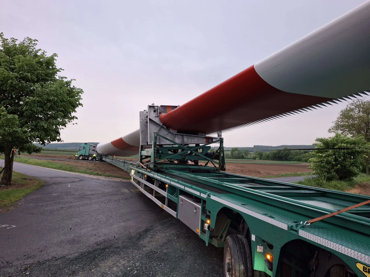 Ein großes rotes und weißes Objekt auf einem Tieflader wird auf einer Straße transportiert.