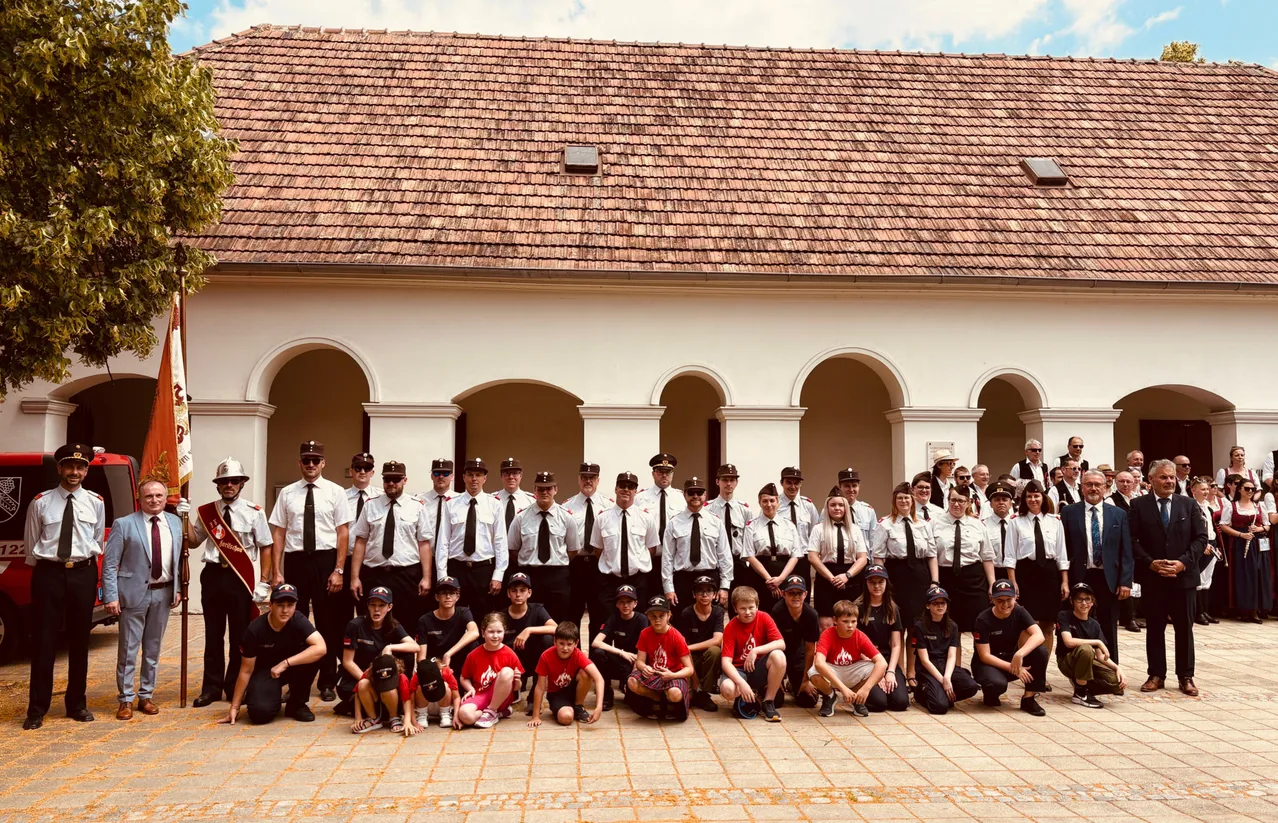 Eine Gruppe von Menschen in weißen und roten Uniformen mit Hüten und Schuhen posiert für ein Foto vor einem Gebäude mit gewölbten Durchgängen.