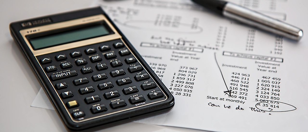 Ein Taschenrechner liegt auf einem Finanzdokument. Daneben ist ein Stift. Das Papier hat Zahlen und Text.