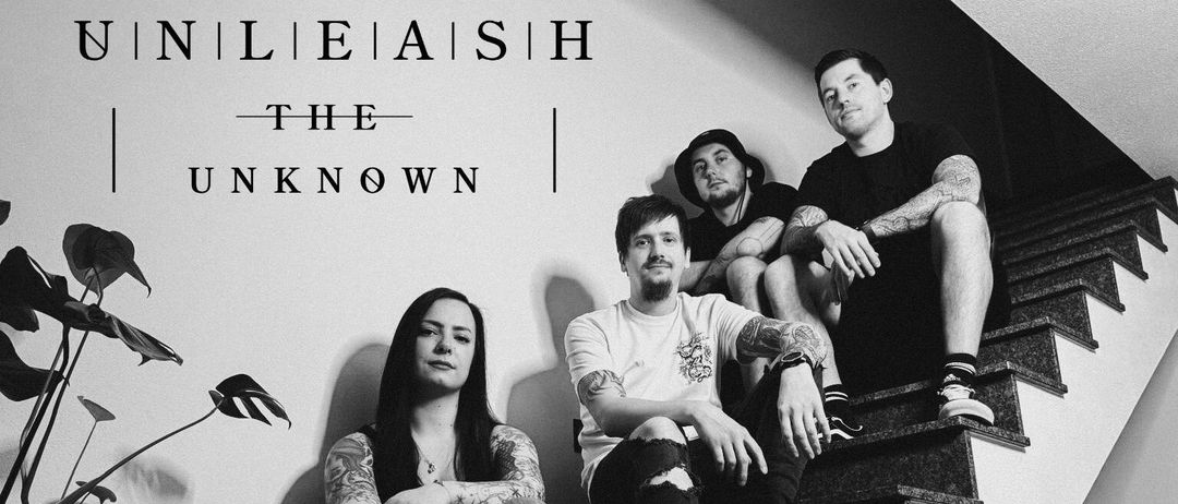 Ein schwarz-weißes Bild zeigt die Band 'Eliash' mit vier tätowierten Mitgliedern, die an einer Wand sitzen. Die Frau links hat lange Haare und trägt ein schwarzes Oberteil.