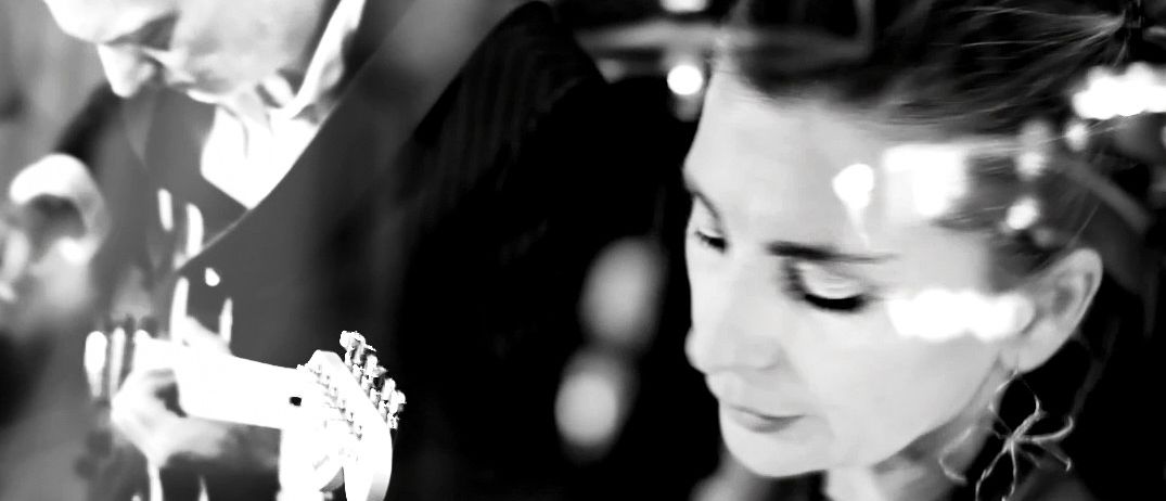 Ein Schwarz-Weiß-Foto zeigt einen Mann, der Gitarre spielt, und eine Frau, die mit einem Mikrofon singt, vor einem verschwommenen Hintergrund.