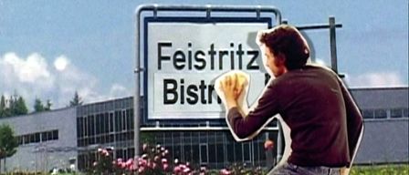 Ein Mann hält ein Schild vor einem Straßenschild für Feisritz Bistro.