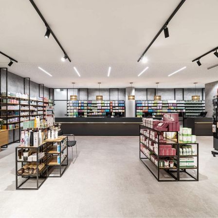 Ein leeres Ladeninneres mit zwei großen schwarzen Regalen, weißem Boden und einer langen Theke. Verschiedene Produkte sind auf den Regalen ausgestellt.
