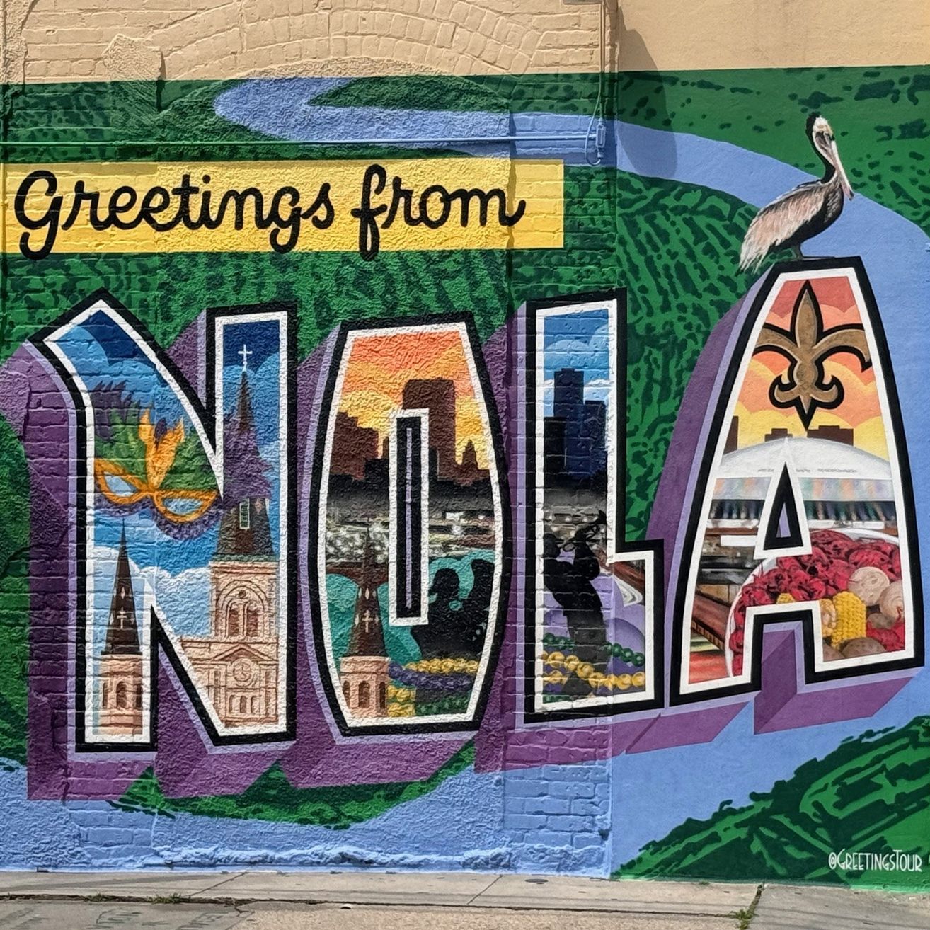Ein Wandbild mit der Aufschrift 'Greetings from NOLA' und einem Pelikan obenauf. Die Buchstaben sind mit Stadtlandschaften, Kathedralen und Essensillustrationen gefüllt.