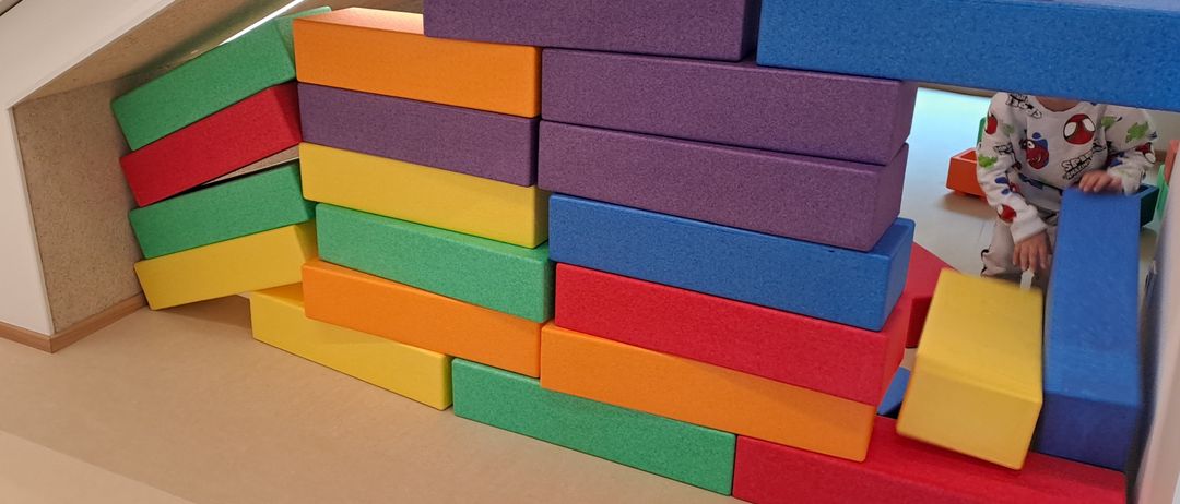 Ein farbenfroher Stapel aus Schaumstoffblöcken auf dem Boden, mit Personen im Hintergrund.