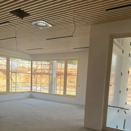 Ein leerer Raum mit großen Fenstern und einer Holzdecke. Der Raum scheint im Bau zu sein.