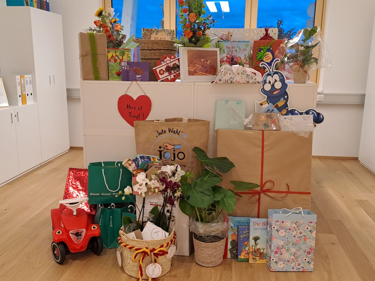 Eine Ausstellung verschiedener Geschenke und Dekorationen auf einem Holzboden, einschließlich Bücher, Blumen, ein rotes Spielzeugauto und ein herzförmiges Schild.