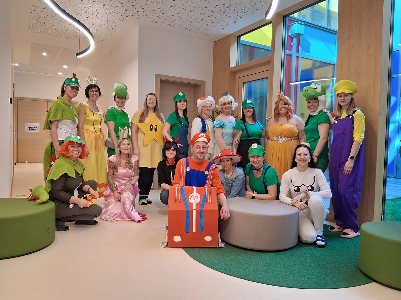 Eine Gruppe von Menschen in verschiedenen Mario-Kostümen posiert für ein Foto in einem Raum. Eine Person trägt einen Mario-Rucksack.