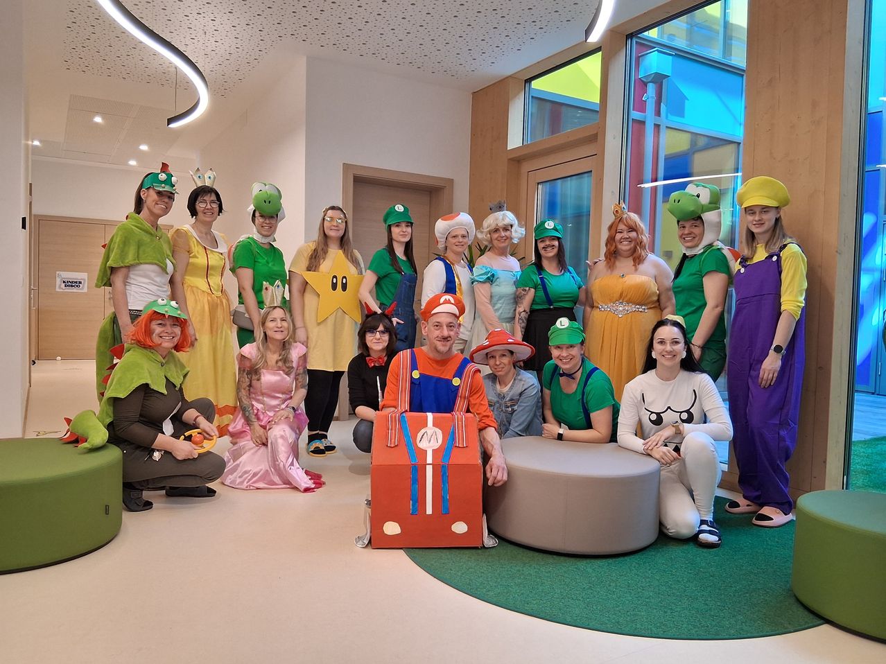 Eine Gruppe von Menschen in verschiedenen Mario-Kostümen posiert für ein Foto in einem Raum. Eine Person trägt einen Mario-Rucksack.