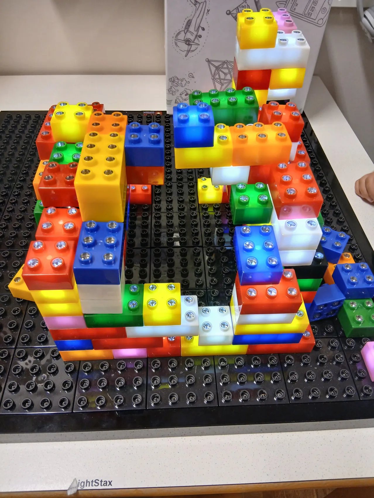 Eine farbenfrohe Anordnung von Lego-Steinen, die eine quadratische Form auf einer schwarzen Grundplatte bilden.
