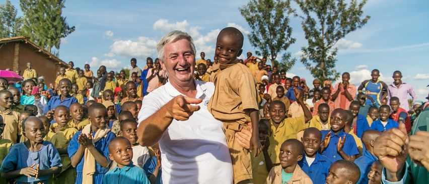 Ein lächelnder älterer Mann hält einen kleinen Jungen in den Armen, umgeben von einer Menge von Kindern.