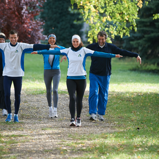 Vier Menschen in Sportkleidung gehen auf einem Kiesweg in einem Park, mit zwei Frauen in der Mitte, eine trägt einen Hijab.