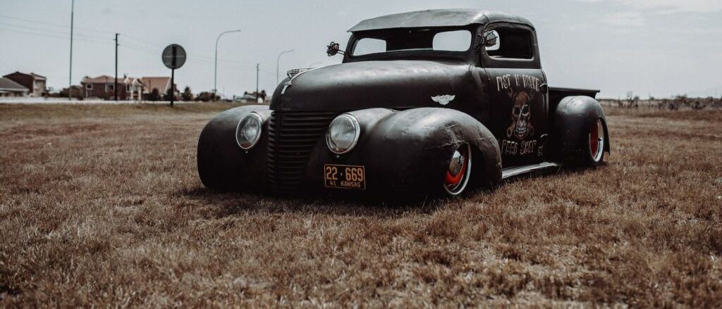 Ein alter schwarzer Pickup-Truck mit Totenkopf-Grafiken und einem Nummernschild mit der Aufschrift 22-669 steht auf einem Grasfeld.