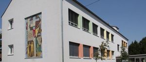 Ein modernes weißes Gebäude mit farbenfrohen Fenstern und einer großen Wandmalerei an der Seite, unter einem klaren blauen Himmel.