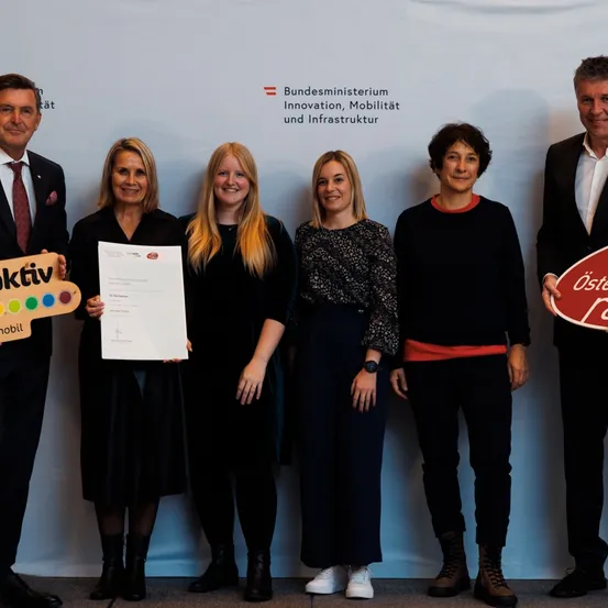 Fünf Personen posieren für ein Foto vor einem weißen Hintergrund mit der Aufschrift 'Bundesministerium Innovation, Mobilität und Infrastruktur'. Sie halten Urkunden und ein Schild mit dem Wort 'aktiv'.