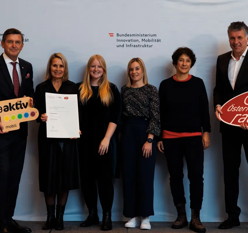 Fünf Personen posieren für ein Foto vor einem weißen Hintergrund mit der Aufschrift 'Bundesministerium Innovation, Mobilität und Infrastruktur'. Sie halten Urkunden und ein Schild mit dem Wort 'aktiv'.