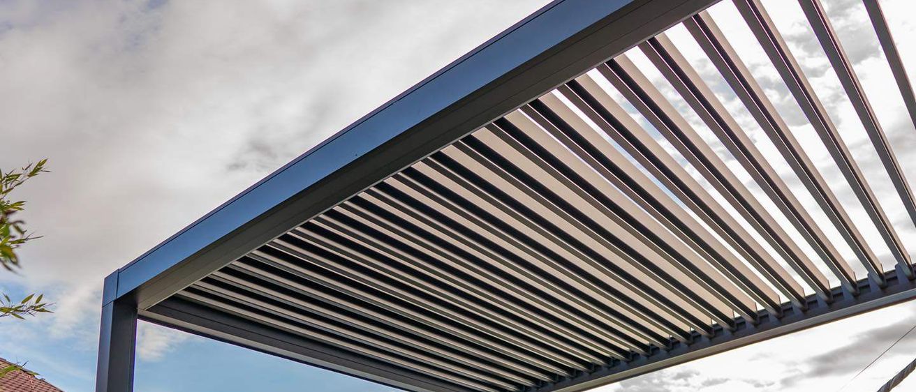 Ein blaues Metalldach mit Lamellen wird von unten betrachtet. Es befindet sich in einer ländlichen Gegend mit Bäumen und Bergen.