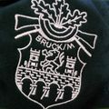 Eine Nahaufnahme eines schwarzen Stoffes mit einem weißen gestickten Wappen. Das Wappen zeigt ein Schlossdesign mit Türmen und einer Schleife. Der Name 'BROCKIN' ist in weißer Stickerei über dem Schloss geschrieben.