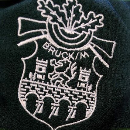 Eine Nahaufnahme eines schwarzen Stoffes mit einem weißen gestickten Wappen. Das Wappen zeigt ein Schlossdesign mit Türmen und einer Schleife. Der Name 'BROCKIN' ist in weißer Stickerei über dem Schloss geschrieben.