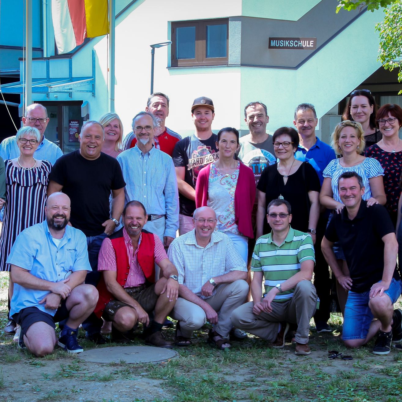 Eine Gruppe von Menschen posiert für ein Foto vor einem Gebäude, das mit Musikschule beschriftet ist.