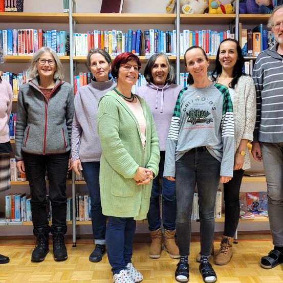 Eine Gruppe von Frauen und Männern steht vor einem Bücherregal und lächelt für ein Foto. Sie tragen alle Winterkleidung.