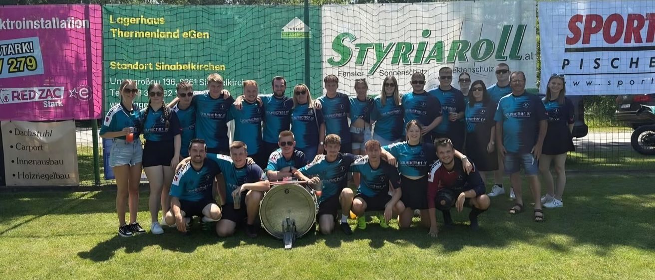 Ein Sportteam in passenden Uniformen steht vor einem Banner mit dem Text 'STYRiARoLL'. Sie halten eine Trommel und posieren für ein Gruppenfoto.