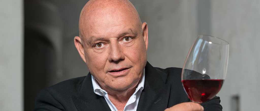 Ein Mann in einem schwarzen Anzug, der ein Glas Rotwein hält. Er scheint ihn zu probieren.