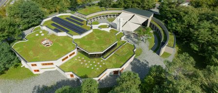 An aerial view of a modern building with a green roof and solar panels. The building is surrounded by trees and grass.