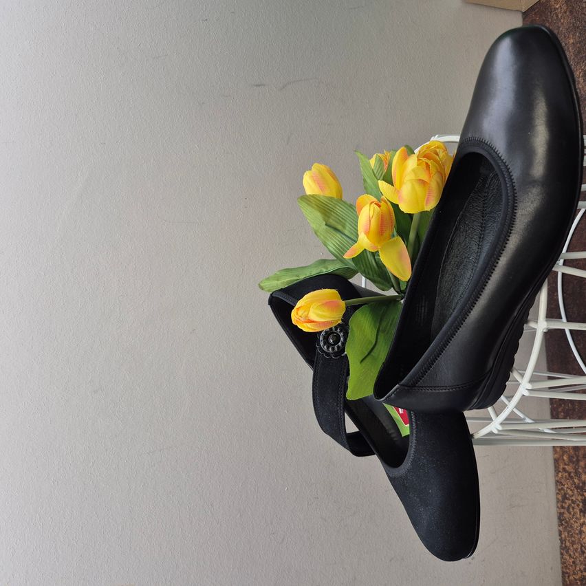 Ein Paar schwarze Lederschuhe hängt an einem weißen Metallständer. Gelbe Tulpen sind im Inneren der Schuhe platziert.