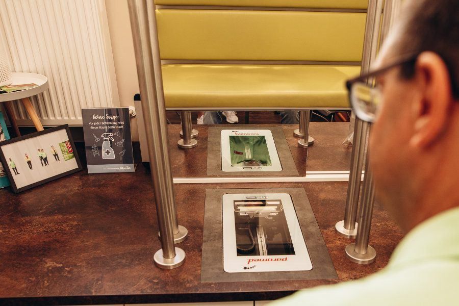 A man wearing glasses is looking at a screen with a picture of a fish on a counter with a yellow bench and a poster behind it.