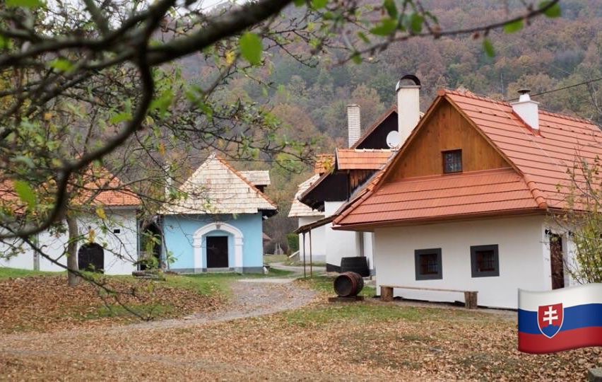 Ein kleines Dorf mit mehreren Häusern, umgeben von Bäumen und Gras, mit einem Berg im Hintergrund.