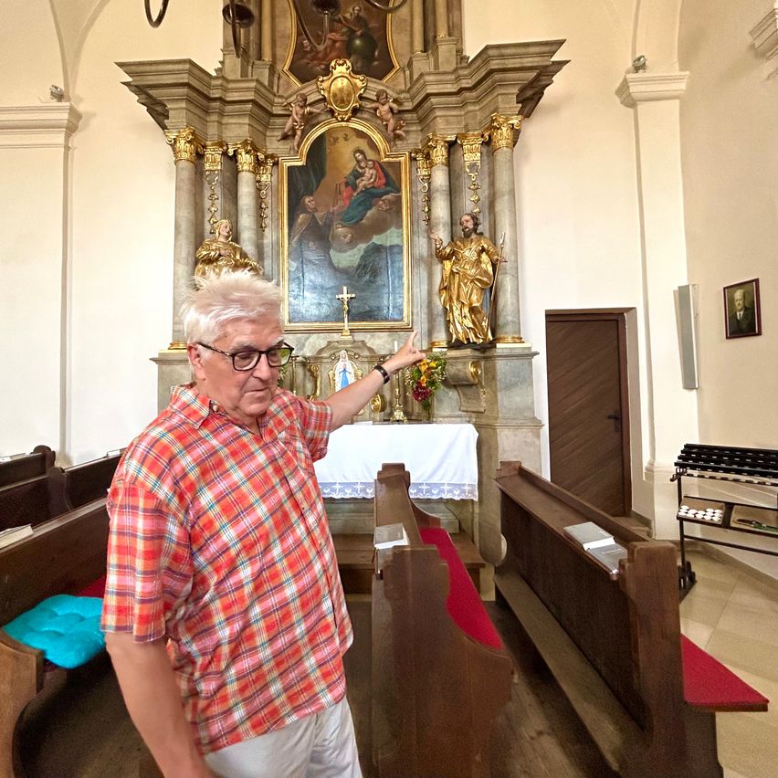 An elderly man points to a painting of the Virgin Mary with Jesus in a church.