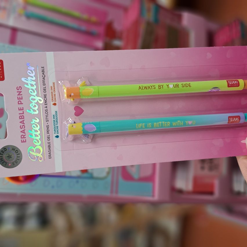 Eine Nahaufnahme von zwei bunten Radiergummis in einer rosa Verpackung. Ein Stift steht 'Immer an deiner Seite' und der andere 'Das Leben ist besser mit dir'. Die Verpackung hat ein glänzendes holografisches Design.