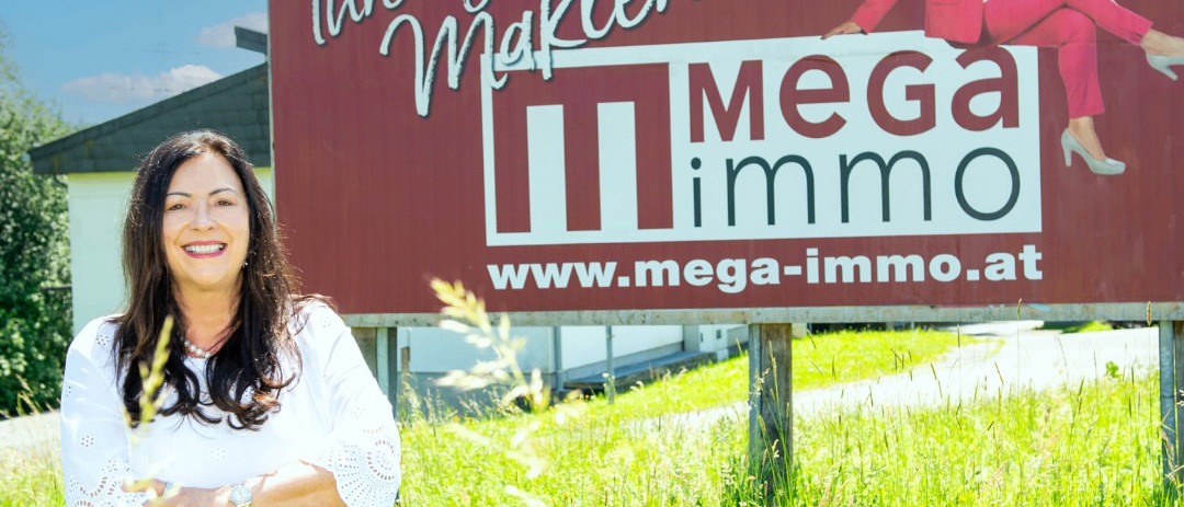 Eine Frau steht vor einem Werbeschild von Mega Immo mit einer lächelnden Frau darauf sitzend.