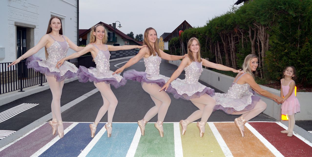 Three female ballet dancers in tutus pose on a multicolored crosswalk. They smile and appear to be enjoying their dance performance.