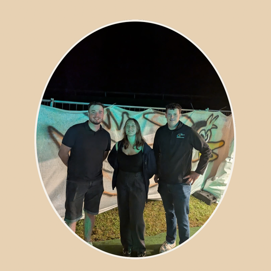 Drei Menschen stehen zusammen vor einer Graffitiwand und lächeln für ein Foto bei Nacht.