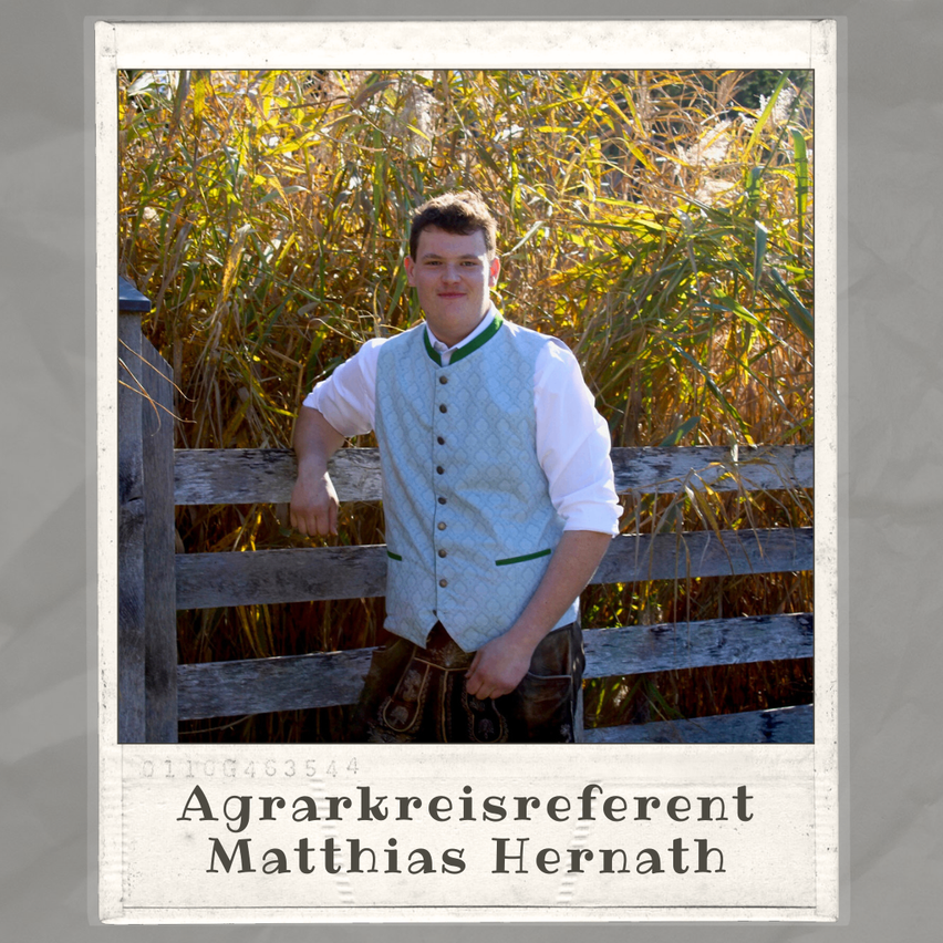 Ein Mann steht neben einem Holzzaun, gekleidet in traditioneller Kleidung, und lächelt in die Kamera. Hinter ihm stehen hohes Gras und ein Holzpfosten. Das Foto hat einen Wasserzeichen mit dem Text 'Agrarkreisereferent Matthias Hernath.'