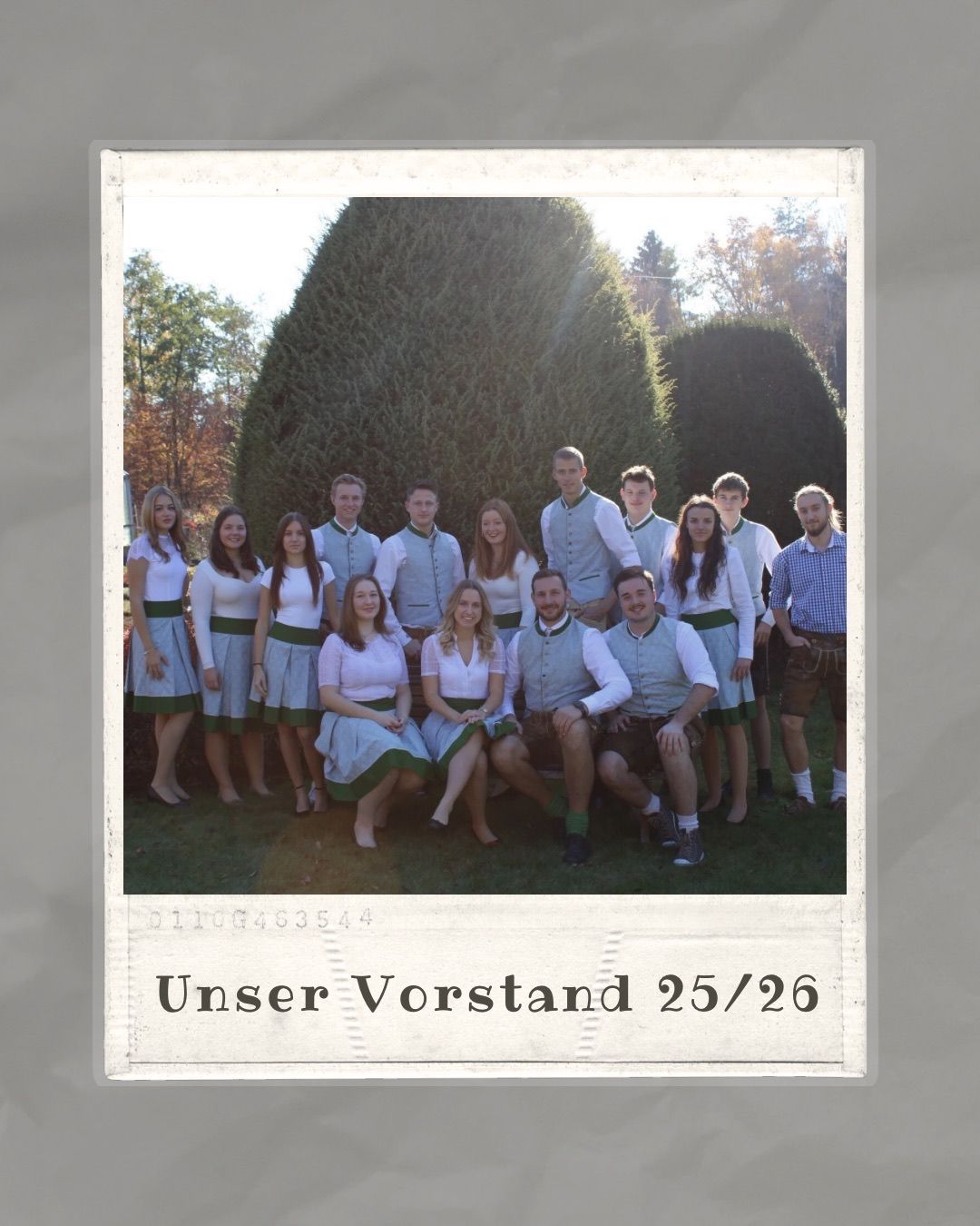 Eine Gruppe von Personen in traditioneller deutscher Kleidung, die auf einem Rasenfeld stehen und sitzen, mit Hecken im Hintergrund. Das Bild hat einen Vintage-Filter und den Text 'Unser Vorstand 25/26'.